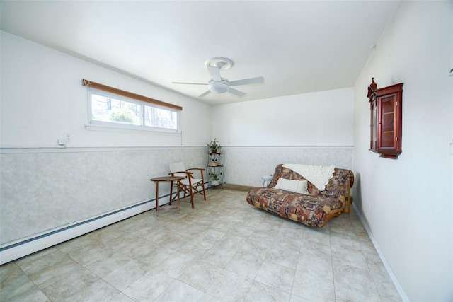 living area with baseboard heating, baseboards, a ceiling fan, and a wainscoted wall