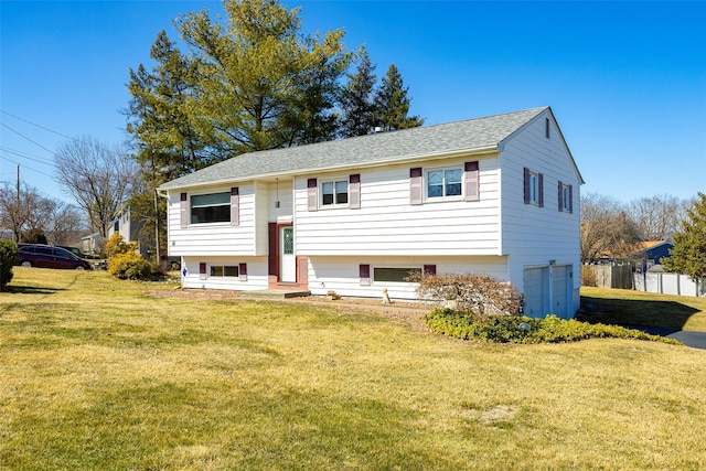 raised ranch with a garage, entry steps, a front yard, and roof with shingles