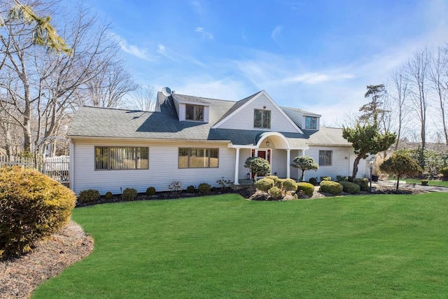 shingle-style home with roof with shingles, a chimney, a front lawn, and fence