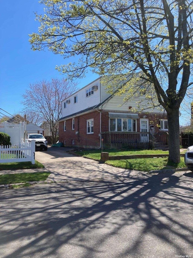 view of front facade with brick siding, driveway, and fence