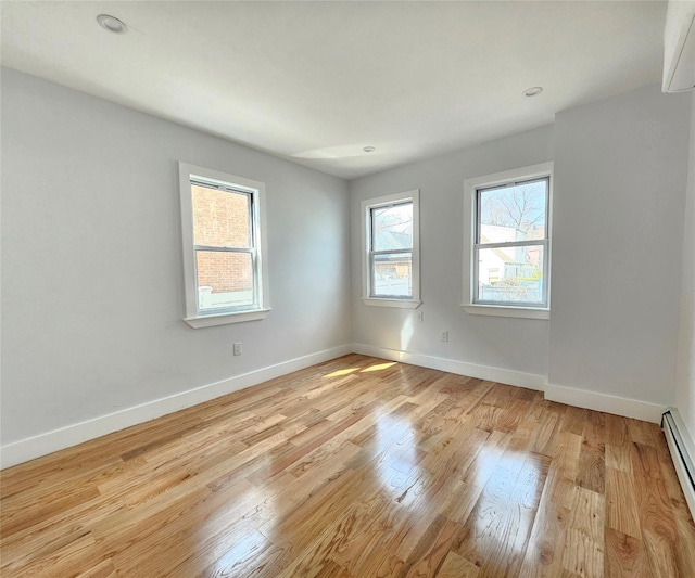 empty room featuring baseboard heating, recessed lighting, light wood-type flooring, and baseboards