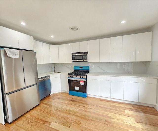 kitchen with appliances with stainless steel finishes, light wood-style flooring, white cabinets, and light countertops