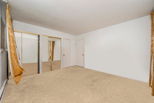 unfurnished bedroom featuring a baseboard heating unit, multiple closets, and carpet floors