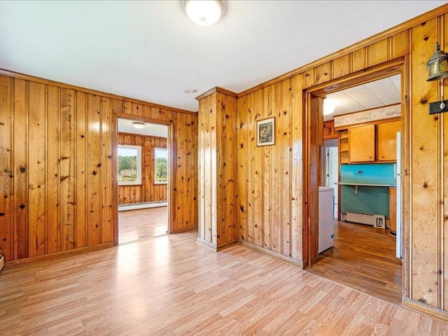 spare room featuring baseboard heating, light wood-type flooring, wooden walls, baseboards, and ornamental molding