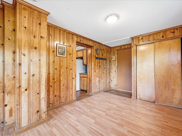 unfurnished bedroom featuring light wood-style floors, wood walls, a closet, baseboards, and refrigerator