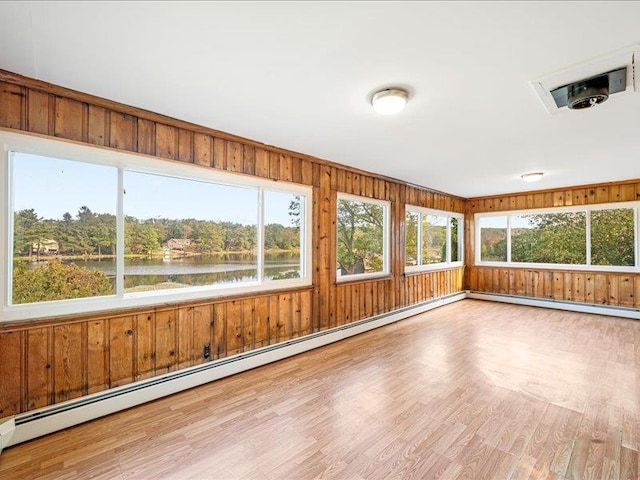 unfurnished sunroom featuring a water view, wood finished floors, wooden walls, a baseboard radiator, and baseboards