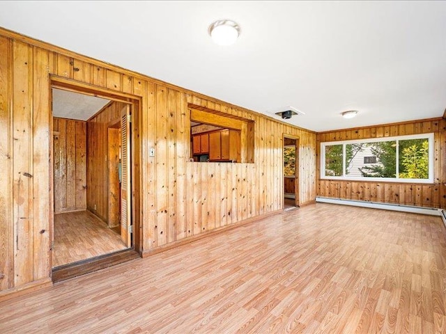 unfurnished living room with light wood-style flooring, wood walls, baseboard heating, baseboards, and ornamental molding