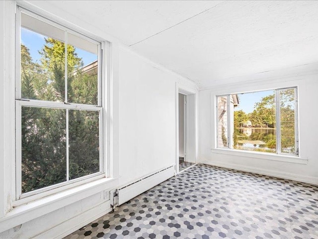 empty room featuring baseboard heating, healthy amount of natural light, and tile patterned floors
