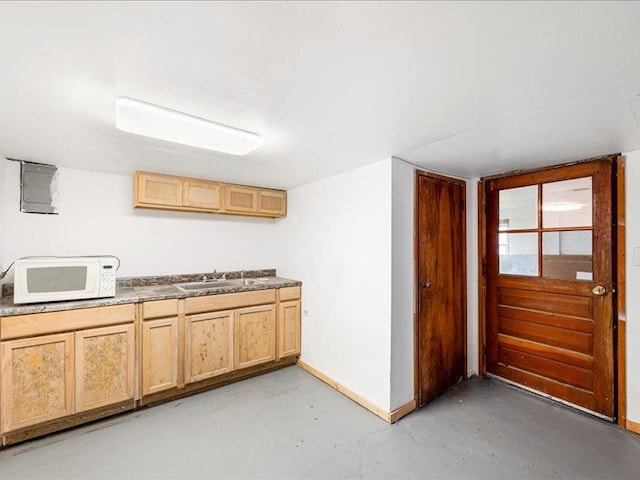 kitchen featuring white microwave, finished concrete floors, a sink, and light brown cabinetry