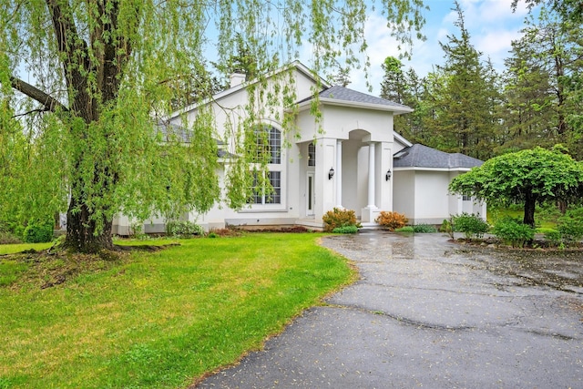 view of front of property with a chimney, stucco siding, a front yard, and driveway