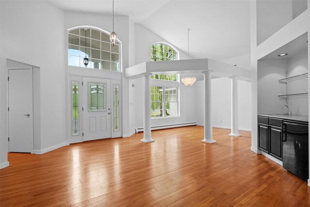foyer entrance featuring ornate columns, a baseboard heating unit, high vaulted ceiling, light wood-style floors, and baseboards