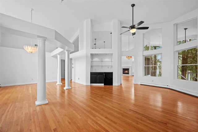 unfurnished living room with ceiling fan, decorative columns, light wood-type flooring, a towering ceiling, and a baseboard heating unit