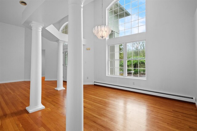 unfurnished living room with a baseboard radiator, light wood-style flooring, ornate columns, baseboards, and a high ceiling