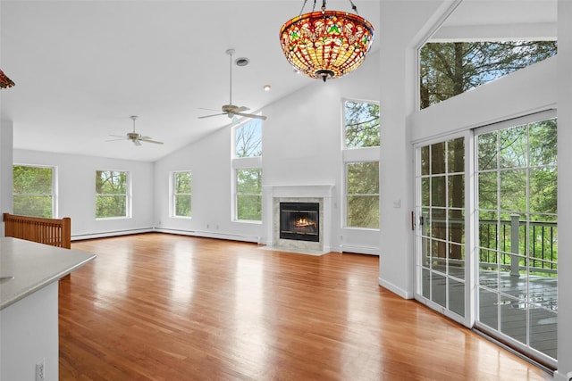 unfurnished living room with high vaulted ceiling, a baseboard heating unit, wood finished floors, a fireplace, and ceiling fan