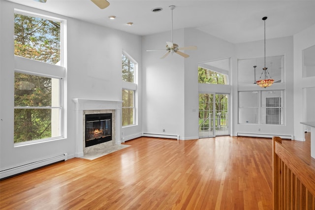 unfurnished living room featuring ceiling fan, a towering ceiling, a baseboard radiator, a premium fireplace, and baseboard heating
