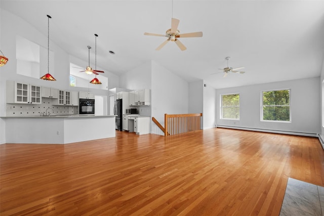 unfurnished living room with a ceiling fan, baseboard heating, high vaulted ceiling, light wood-style floors, and a sink
