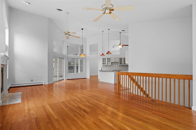 unfurnished living room featuring a ceiling fan, a baseboard heating unit, high vaulted ceiling, light wood finished floors, and a tile fireplace