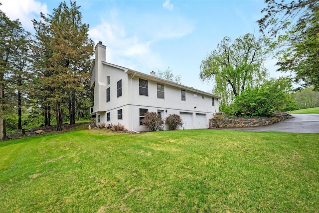 back of house featuring a garage, stucco siding, a chimney, a lawn, and driveway