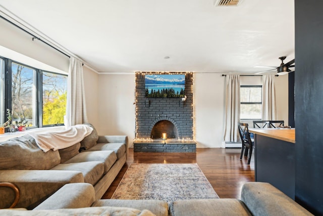 living area featuring ceiling fan, a baseboard heating unit, wood finished floors, and a fireplace