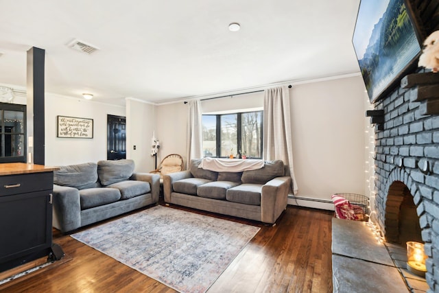 living area with visible vents, dark wood-type flooring, a baseboard heating unit, crown molding, and a brick fireplace