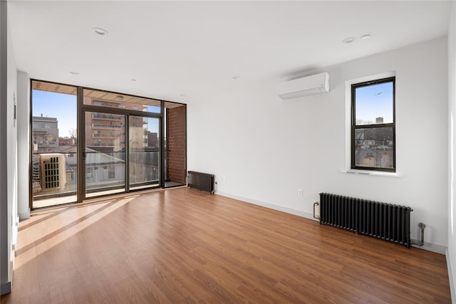 empty room with a wall mounted AC, expansive windows, wood finished floors, radiator heating unit, and baseboards