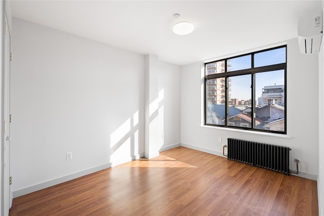 spare room featuring a wall unit AC, radiator, wood finished floors, and baseboards