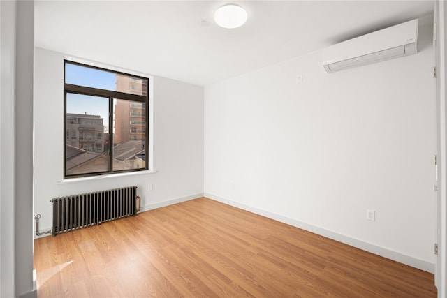 spare room featuring a wall unit AC, radiator heating unit, wood finished floors, and baseboards