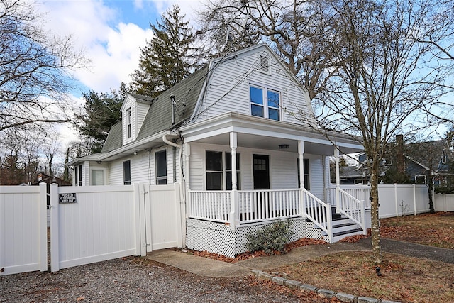 view of front facade featuring a gambrel roof, a gate, a porch, fence, and a shingled roof