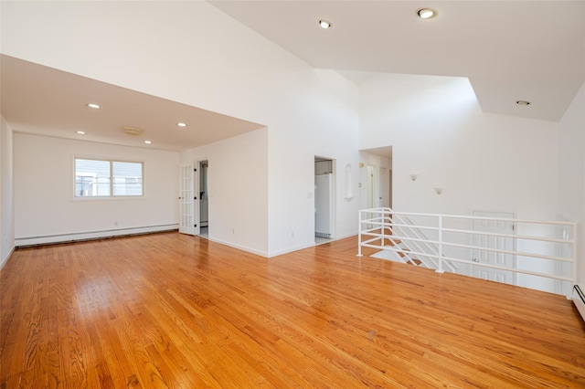 empty room featuring baseboards, a baseboard radiator, a high ceiling, recessed lighting, and light wood-style floors