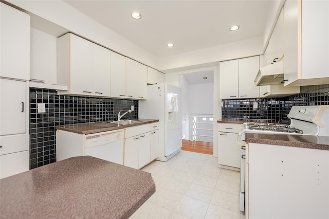 kitchen featuring dark countertops, under cabinet range hood, white appliances, white cabinetry, and a sink