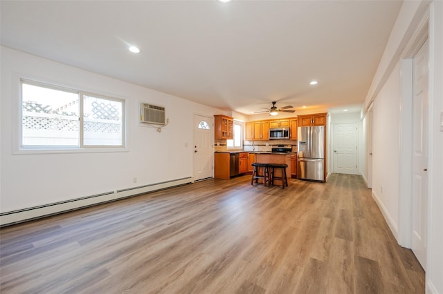 kitchen featuring a wall mounted air conditioner, appliances with stainless steel finishes, brown cabinetry, light wood finished floors, and a baseboard radiator