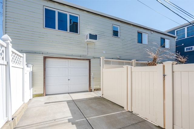 back of property with an attached garage, concrete driveway, a wall unit AC, and fence