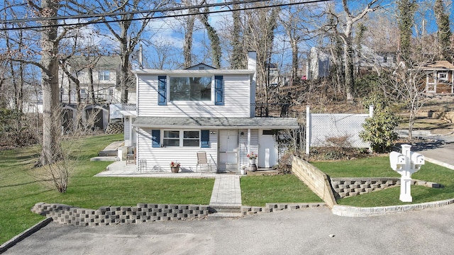 traditional home featuring a balcony, a shingled roof, a front yard, and fence