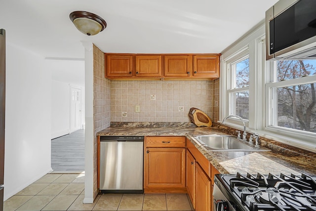 kitchen with light tile patterned flooring, a sink, appliances with stainless steel finishes, brown cabinets, and backsplash