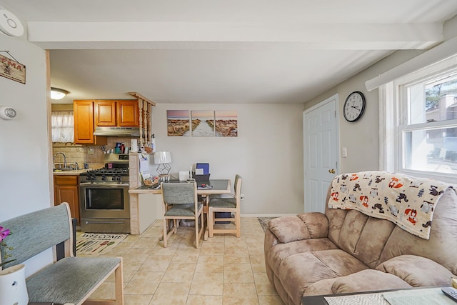 kitchen featuring under cabinet range hood, a sink, stainless steel range with gas cooktop, light tile patterned floors, and decorative backsplash