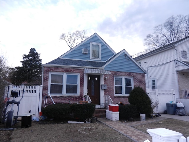 bungalow-style home featuring brick siding, a wall unit AC, roof with shingles, and fence