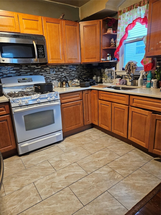 kitchen with brown cabinetry, a sink, light countertops, stainless steel microwave, and white gas range