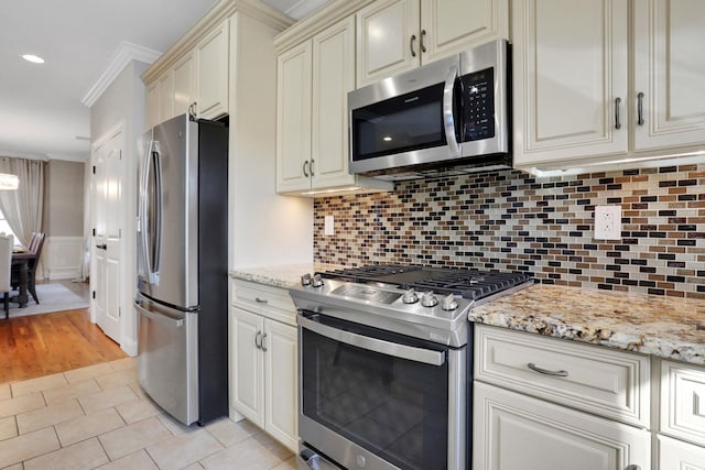 kitchen featuring cream cabinetry, tasteful backsplash, stainless steel appliances, light tile patterned flooring, and crown molding