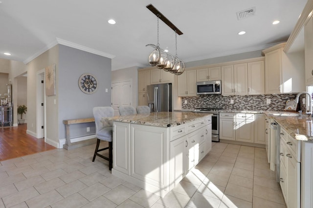 kitchen with visible vents, a kitchen island, a sink, stainless steel appliances, and cream cabinetry