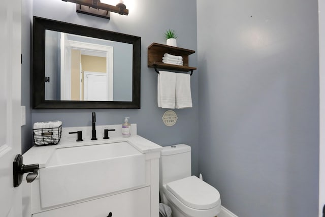 half bath with baseboards, toilet, and vanity