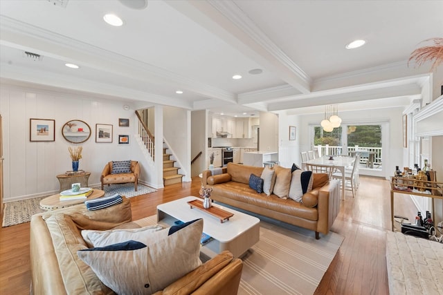 living room featuring beamed ceiling, visible vents, ornamental molding, light wood finished floors, and stairs