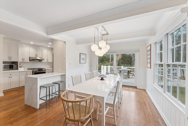 dining area with light wood-style flooring, ornamental molding, beamed ceiling, and wainscoting