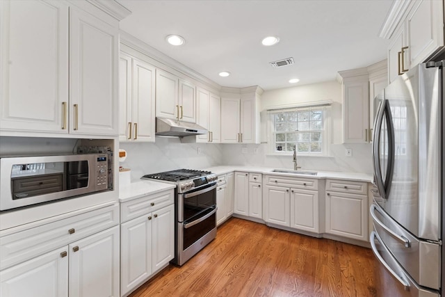 kitchen with under cabinet range hood, light countertops, appliances with stainless steel finishes, white cabinetry, and a sink