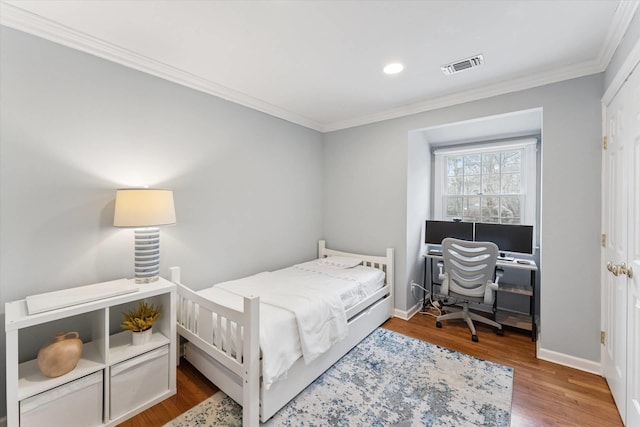 bedroom featuring visible vents, baseboards, wood finished floors, and ornamental molding