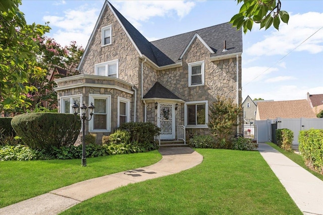 view of front of property featuring fence, roof with shingles, a front yard, stone siding, and a gate