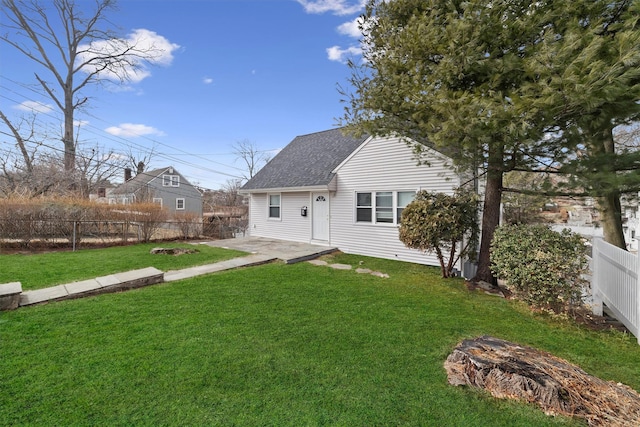 rear view of property featuring a lawn, a fenced backyard, and roof with shingles