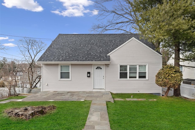 view of front of house with a patio, a shingled roof, a front yard, and fence