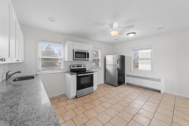 kitchen featuring radiator heating unit, light stone counters, white cabinets, stainless steel appliances, and a sink