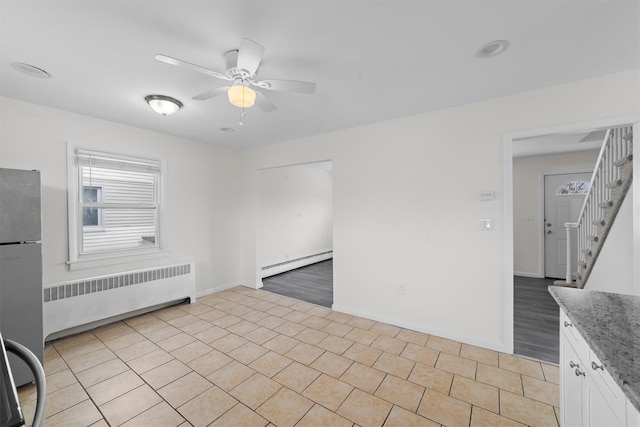 interior space featuring a ceiling fan, radiator heating unit, light tile patterned flooring, baseboard heating, and stairs