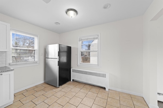 kitchen with baseboards, radiator heating unit, freestanding refrigerator, light tile patterned flooring, and white cabinets